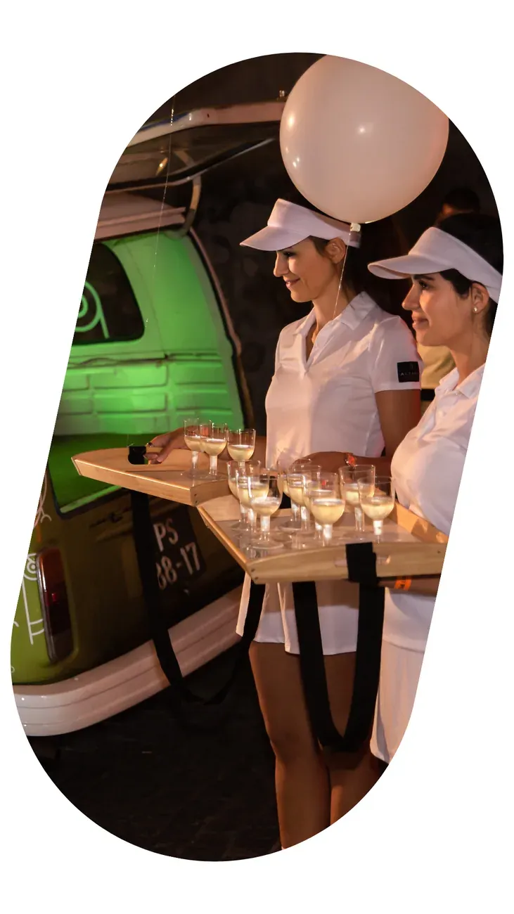 Waitresses serving canapés beside a vintage green van decorated with balloons.