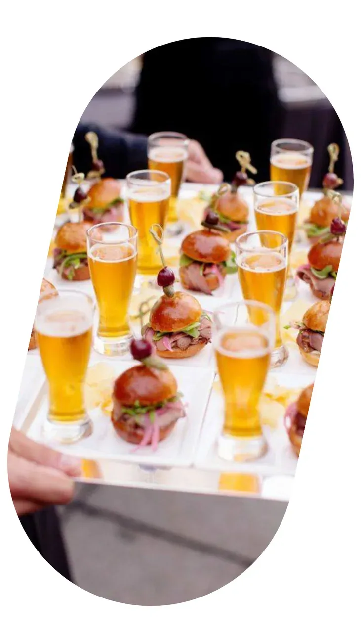 A tray of sliders and glasses of beer, served standing at a cocktail.