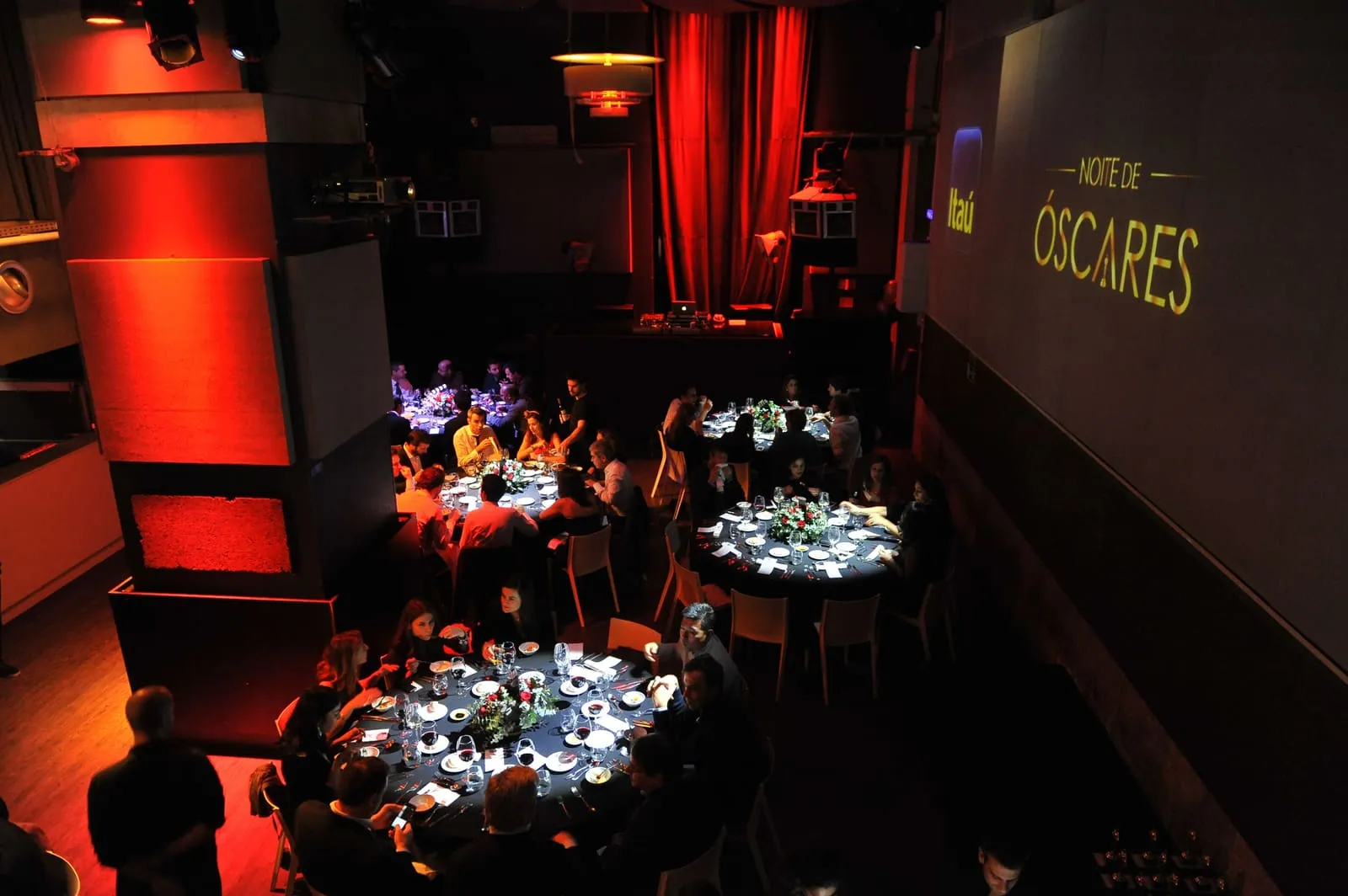 Dinner under red light, with an "Óscares" sign projected on the far wall.