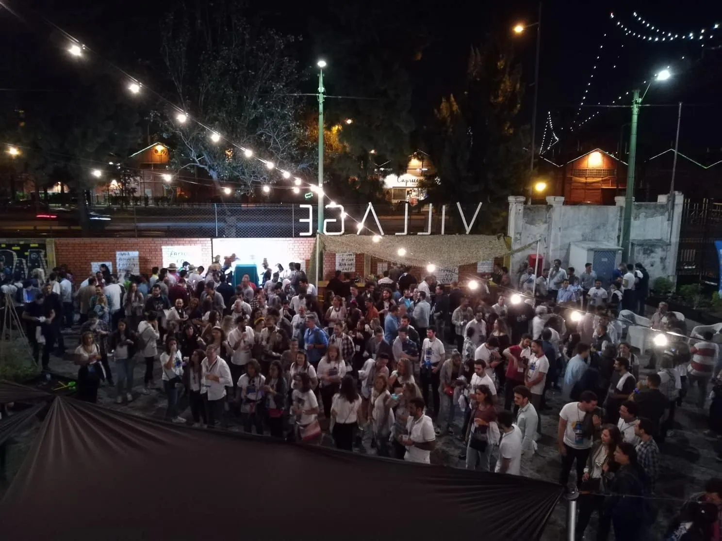 An outdoor party at night, festoon lights strung above a crowd.