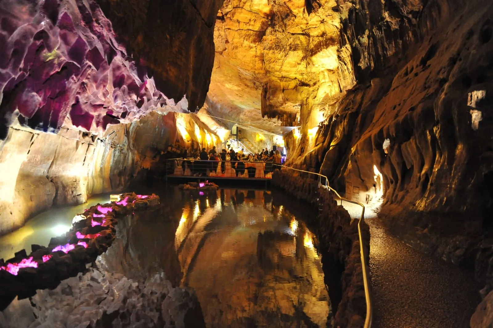 Jantar dentro de uma gruta, com a rocha iluminada a dourado e rosa a reflectir-se num lago, e pétalas espalhadas pela margem.