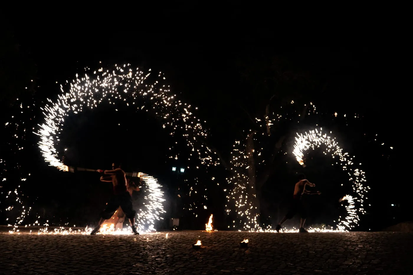 Dois artistas de fogo a girar rodas de faíscas na noite.