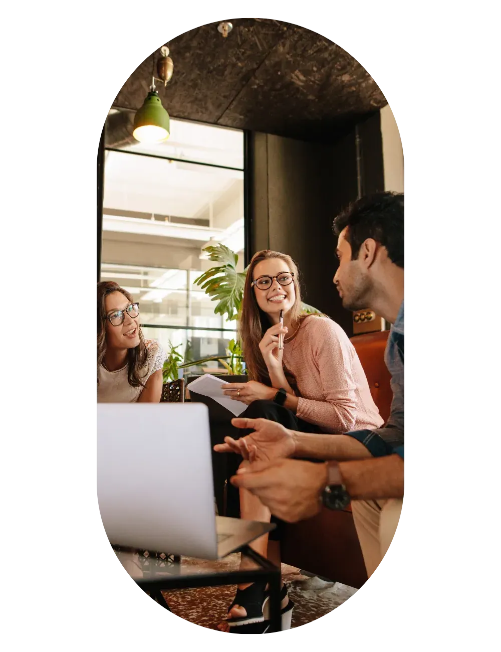 A group around a table with a laptop, discussing ideas in a room full of plants.