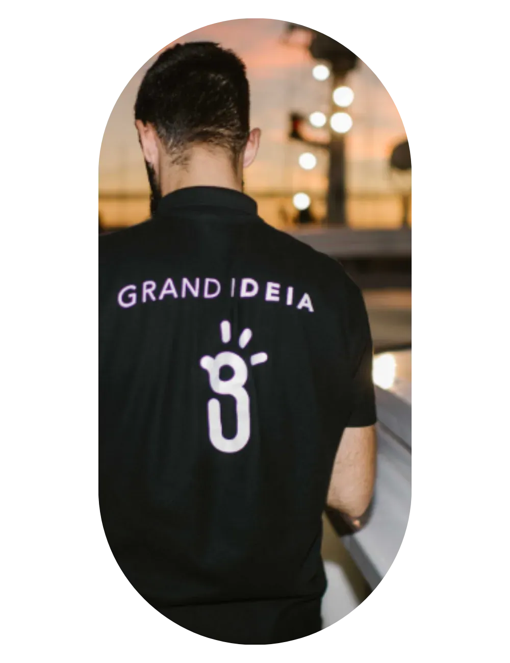 Um membro da equipa Grand'Ideia de costas, com o logotipo na t-shirt, a coordenar um evento no local.