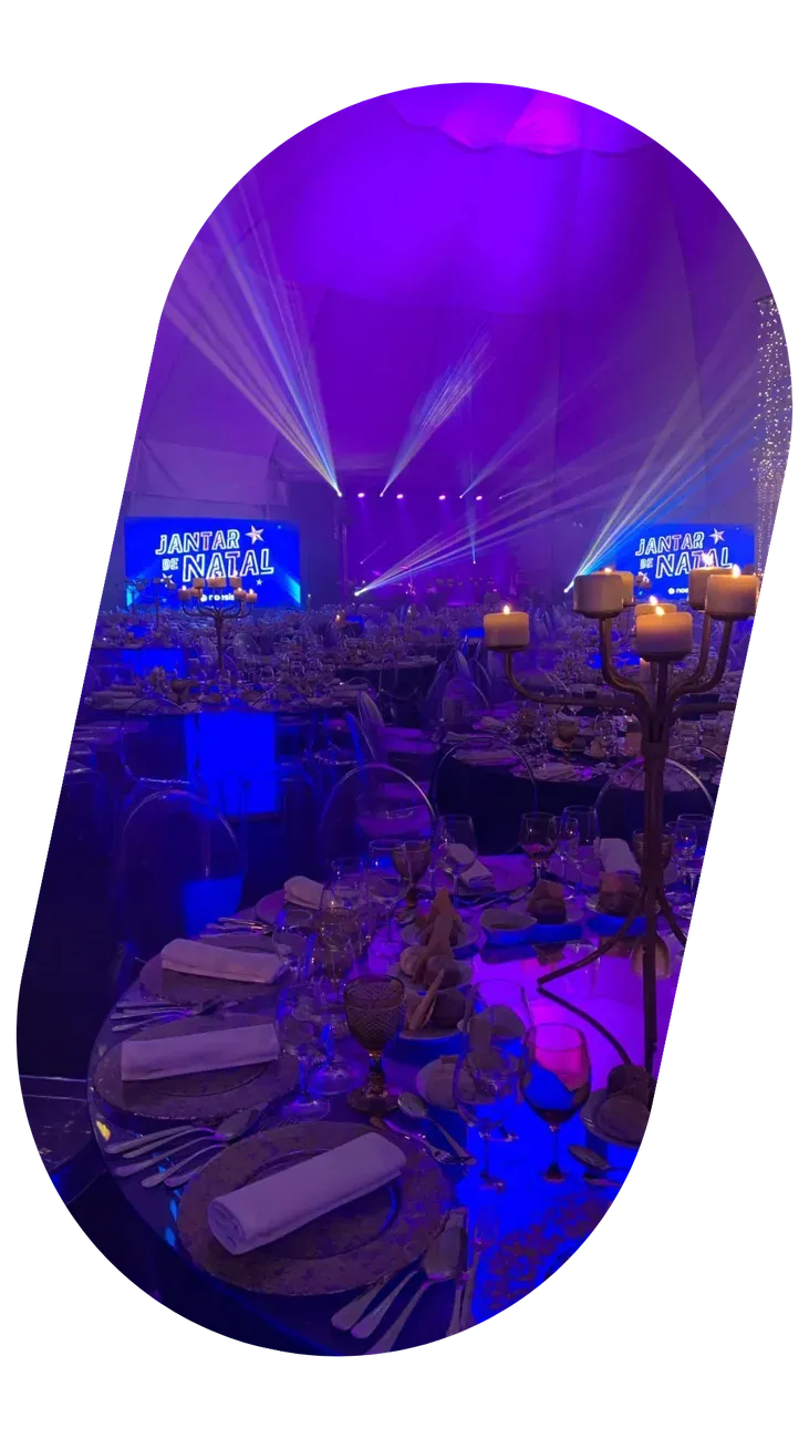 Salão iluminado a roxo e azul durante um jantar de gala, visto do alto.