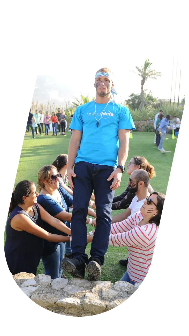 Dinamizador de camisola azul a orientar um grupo sentado em roda, ao ar livre.
