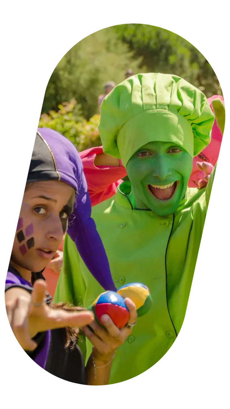 Artistas de fato verde, maquilhados, a fazer malabarismo num parque.