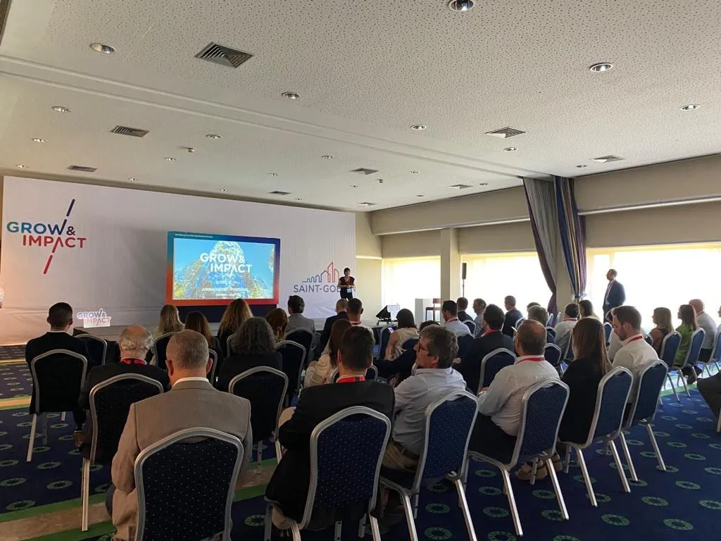 A full conference room, with the Grow & Impact backdrop and the slides on screen.