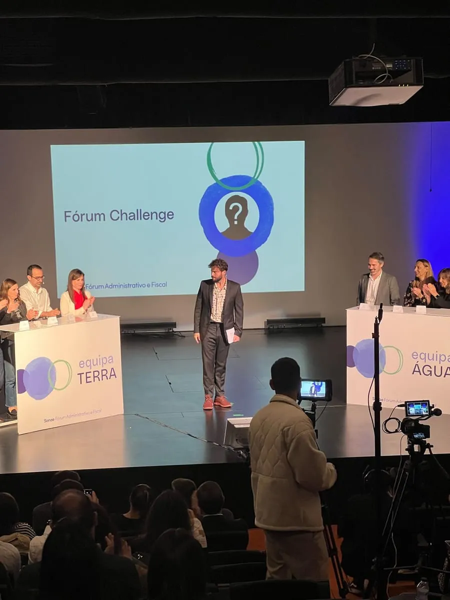 A forum on stage, with two teams at lecterns and a host in the middle.