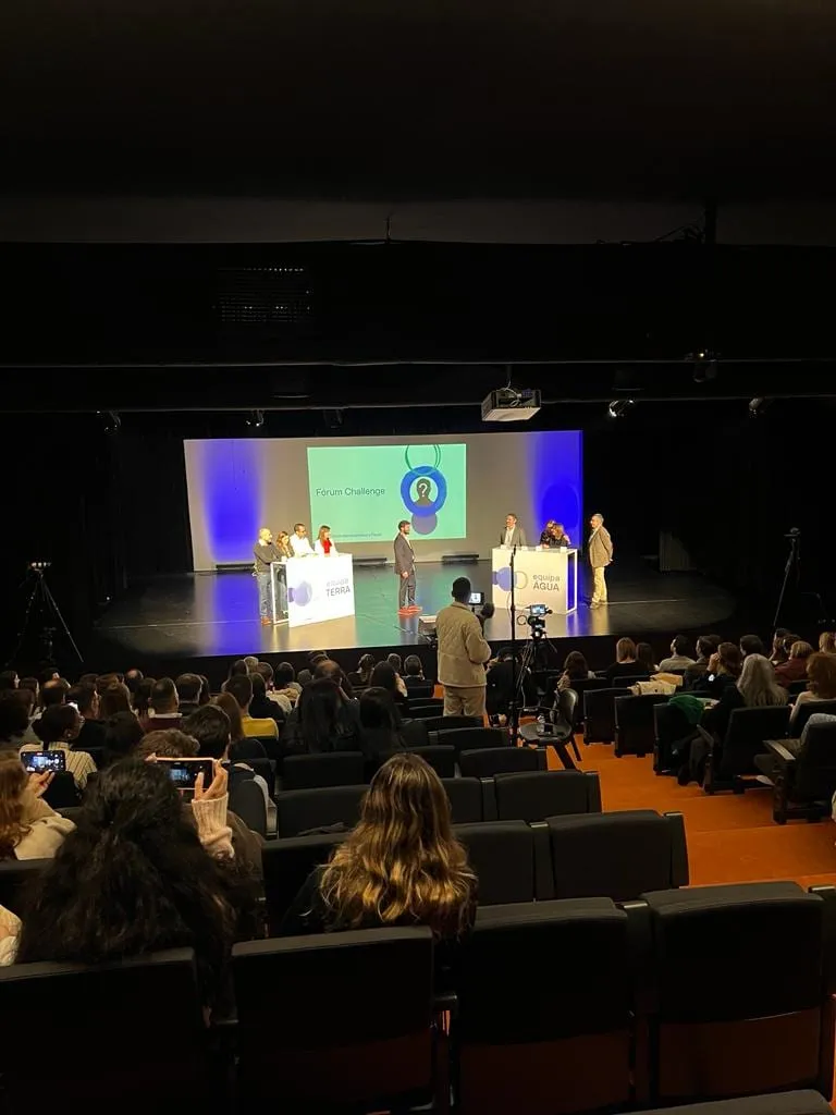 A darkened auditorium, the stage lit in blue and the audience watching.