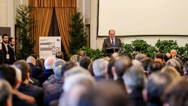 A speaker at a lectern facing a full room, with Christmas trees behind him.