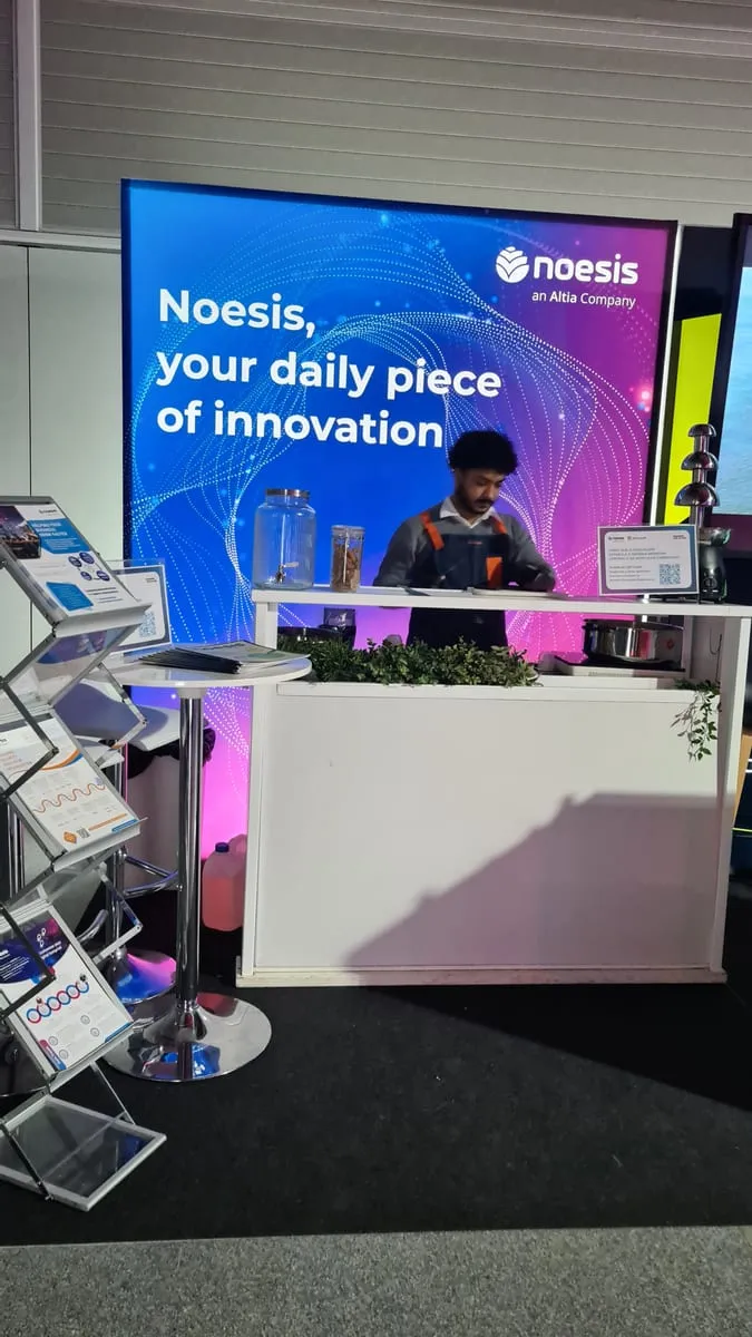A presenter at a stand with screens, in the exhibition area of an innovation event.