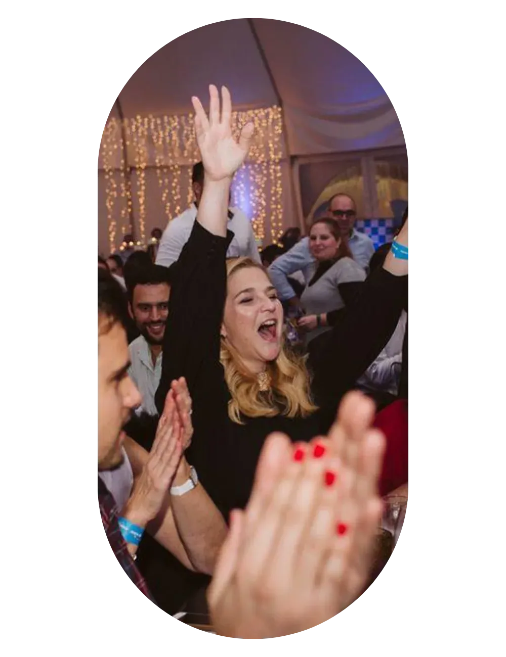 Guests with their arms in the air, laughing and applauding in a hall strung with fairy lights.